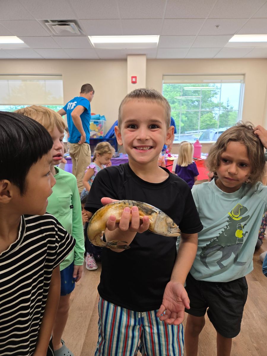 A smiling boy holding a model fish with friends around him