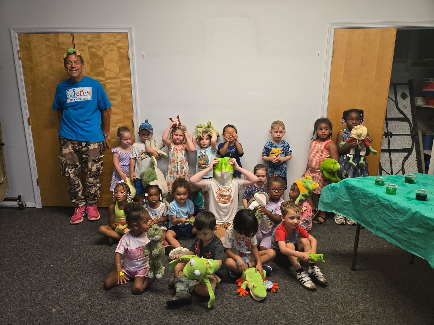 A class sitting together holding green frog toys, with Jack standing behind them