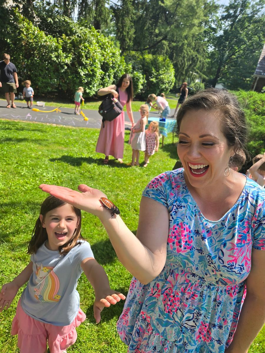 A laughing teacher and a girl playing with a toy frog outdoors