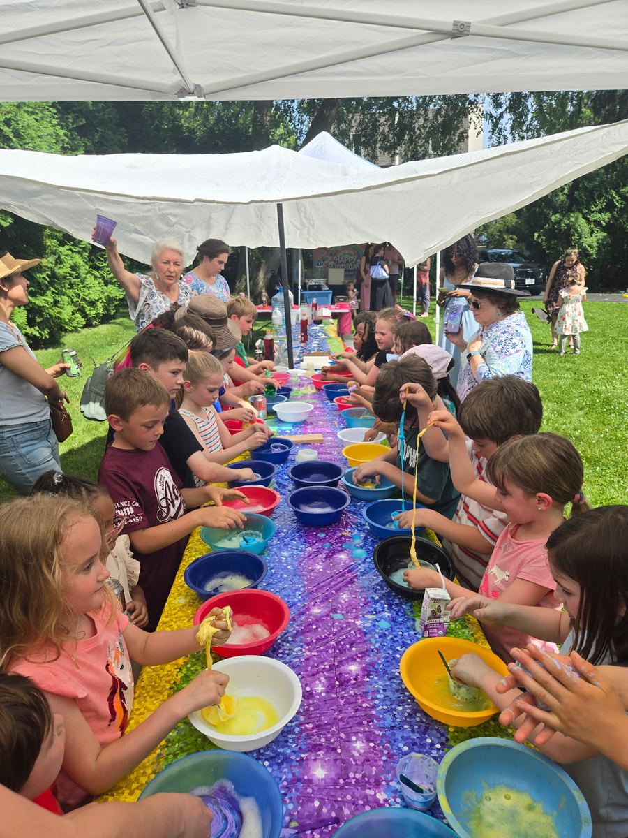 A long outdoor table of children scooping in colorful bowls