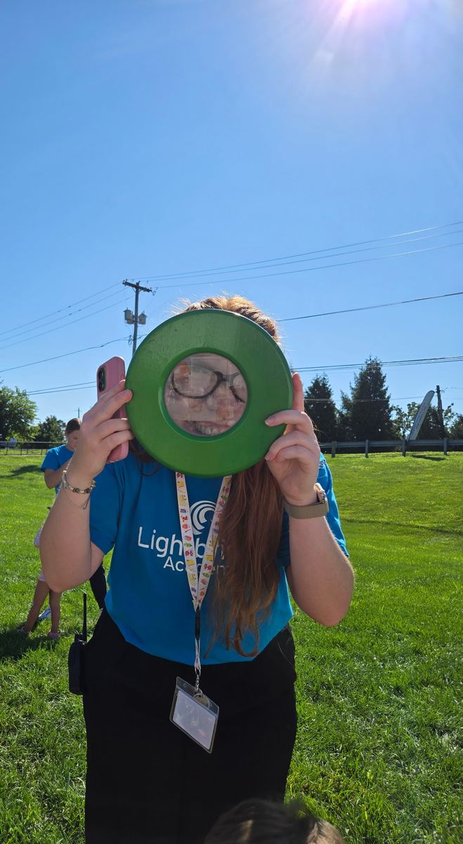 A teacher peeking through a big green magnifying glass