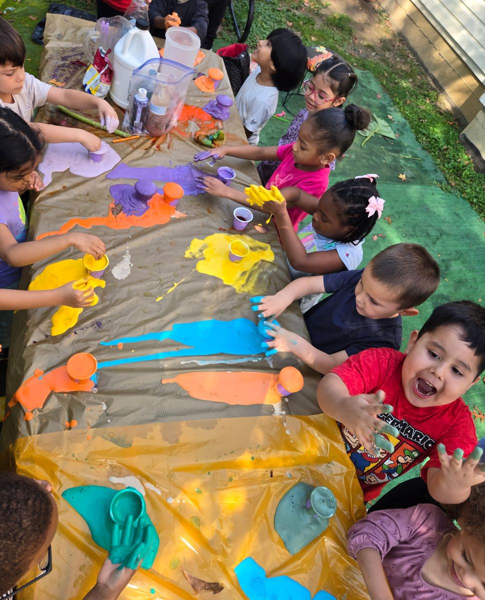 Preschoolers painting with bright colors at a covered table