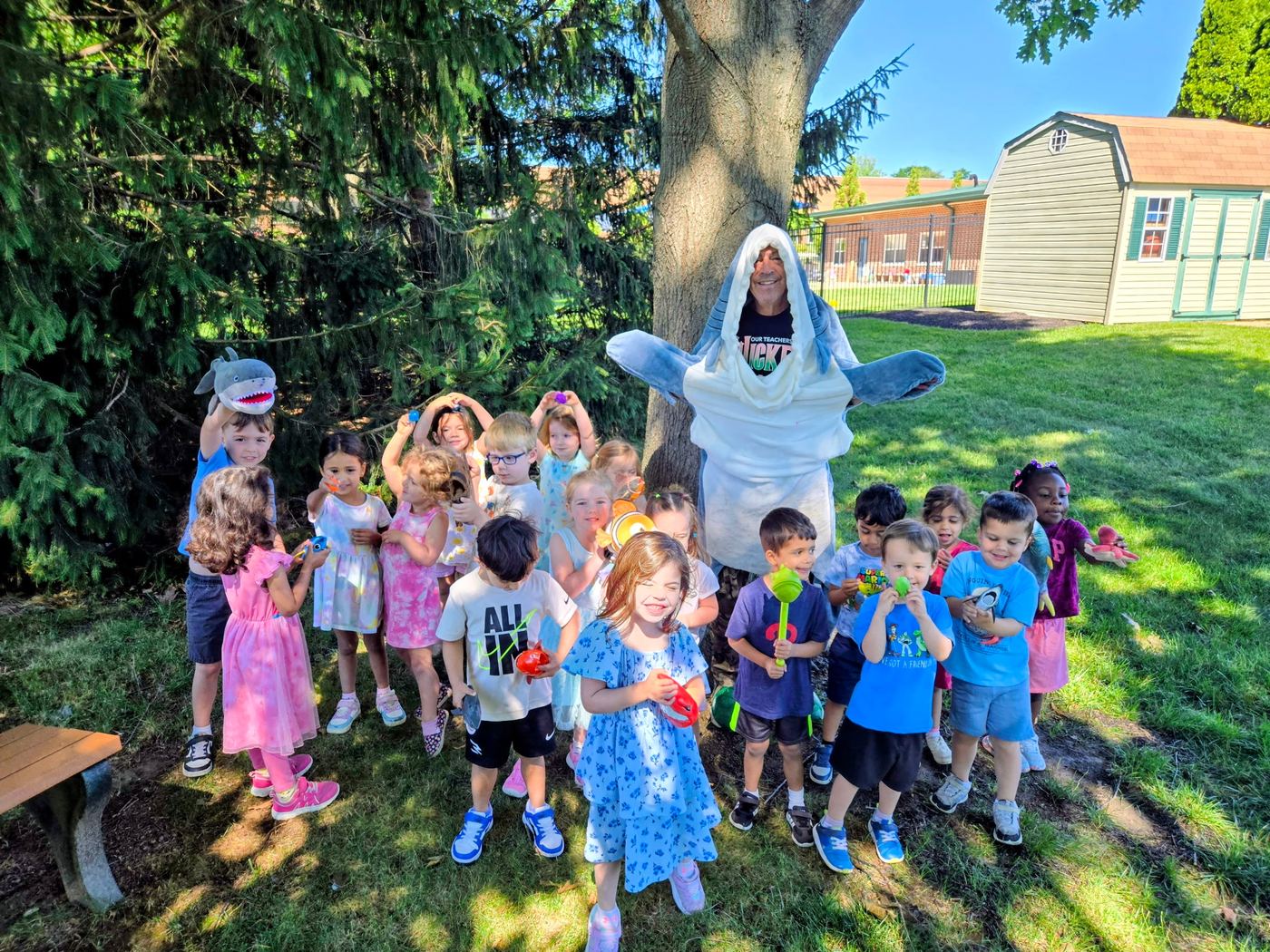 A big group of preschoolers outdoors with a teacher in a shark costume