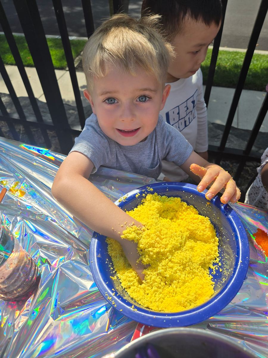 A smiling boy digging his hands into a bowl of yellow sensory material