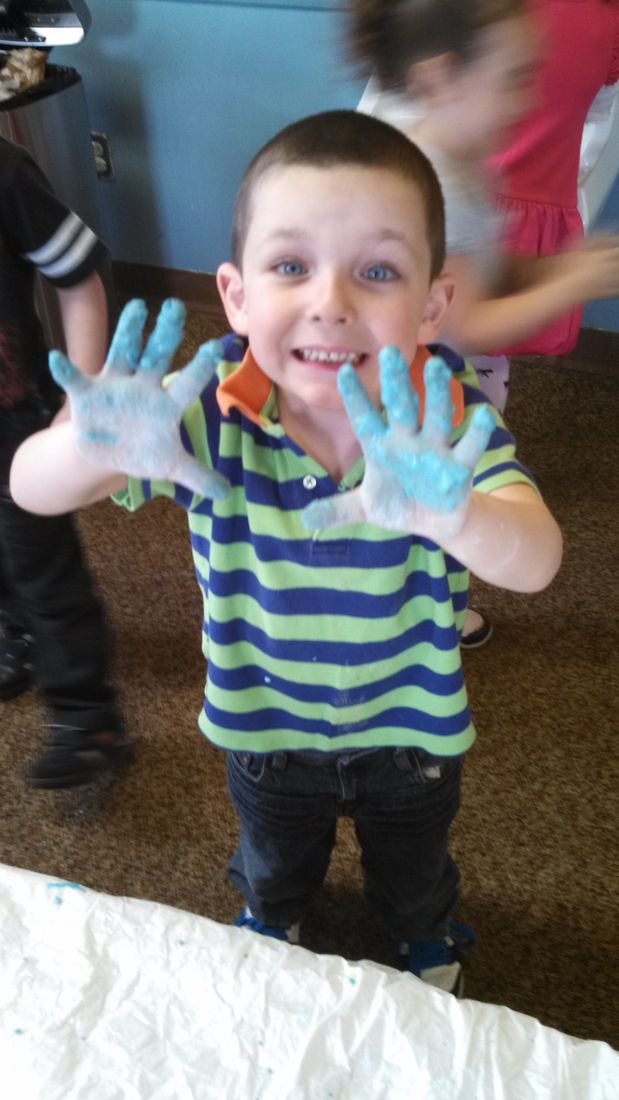 A grinning boy holding up two hands covered in blue goo
