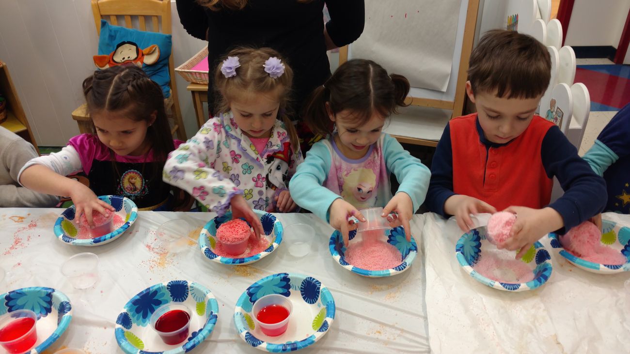 Four preschoolers at a table mixing pink powder in paper bowls