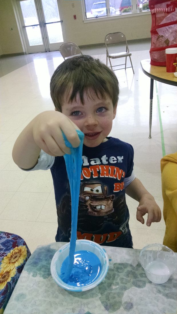 A preschooler stretching a strand of blue slime over a bowl