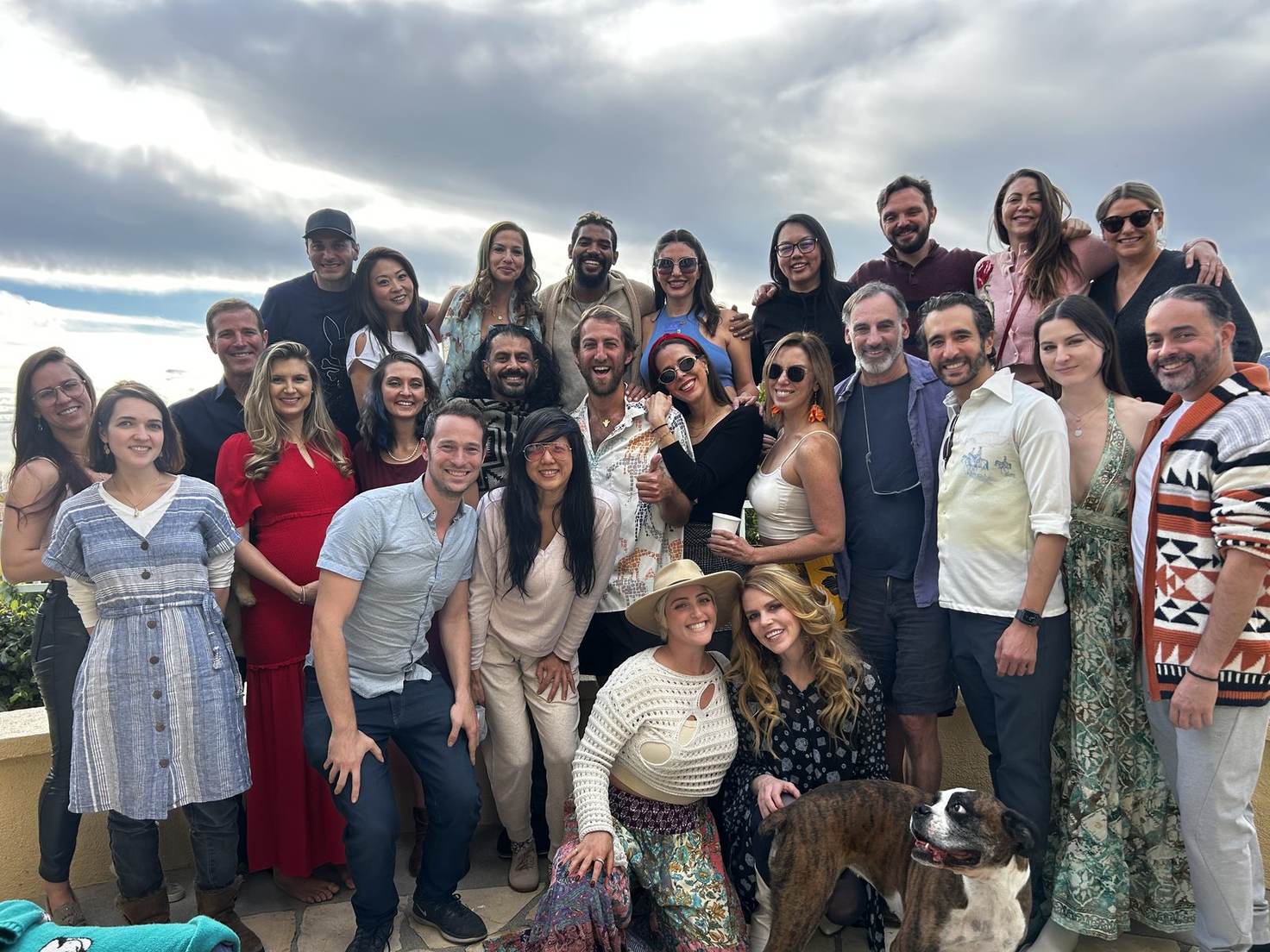 About twenty-seven Giraffes and a dog posed together on a terrace at Friendsgiving